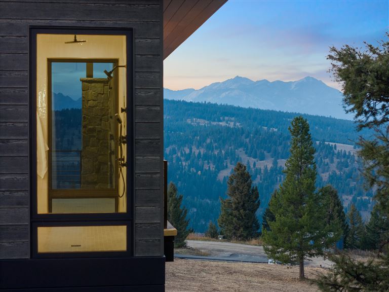 Wooden cabin by a snowy mountain lake at dawn.