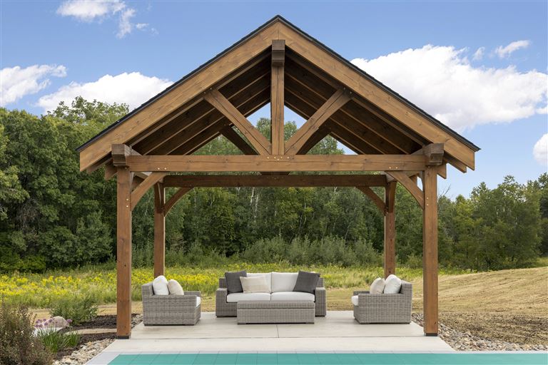 Luxury wooden gazebo in a family garden with trees and a clear sky.