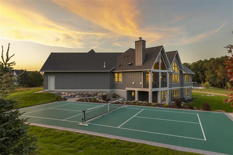 Luxurious mansion with a private tennis court and lush lawn at twilight.