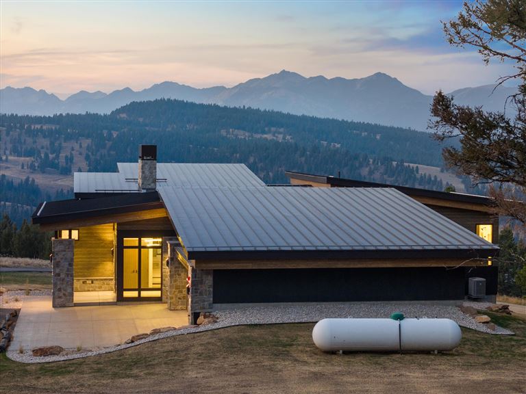 Wooden cabin by a lake in a snowy landscape with trees and clear sky.