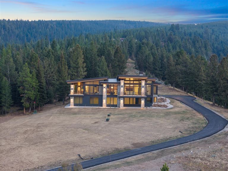 Scenic view of a mountain valley with a cabin, lake, and trees.