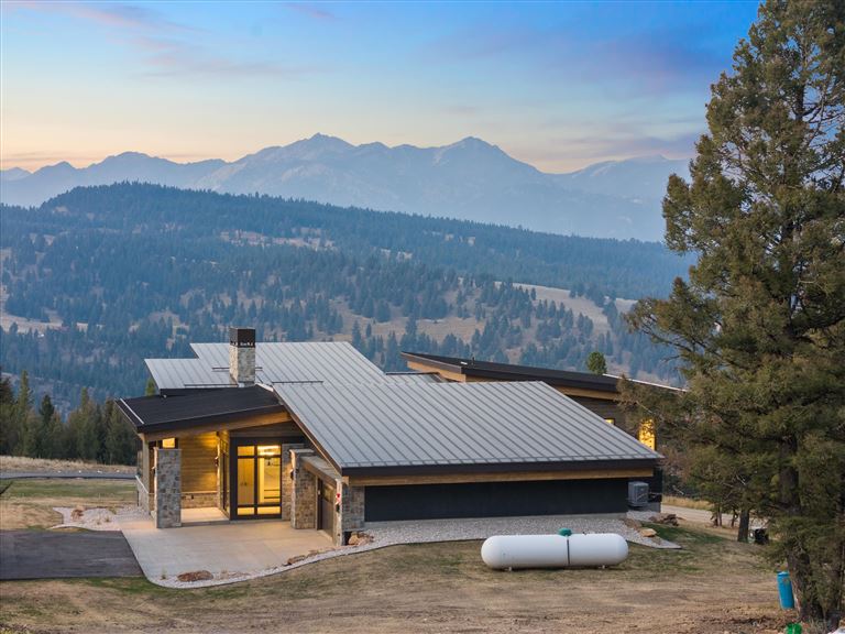 Wooden cabin in a mountain landscape with snow-capped peaks and a lake.