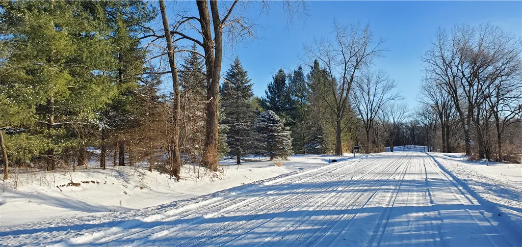 Snow-covered road through a winter landscape at dawn with frosty trees.